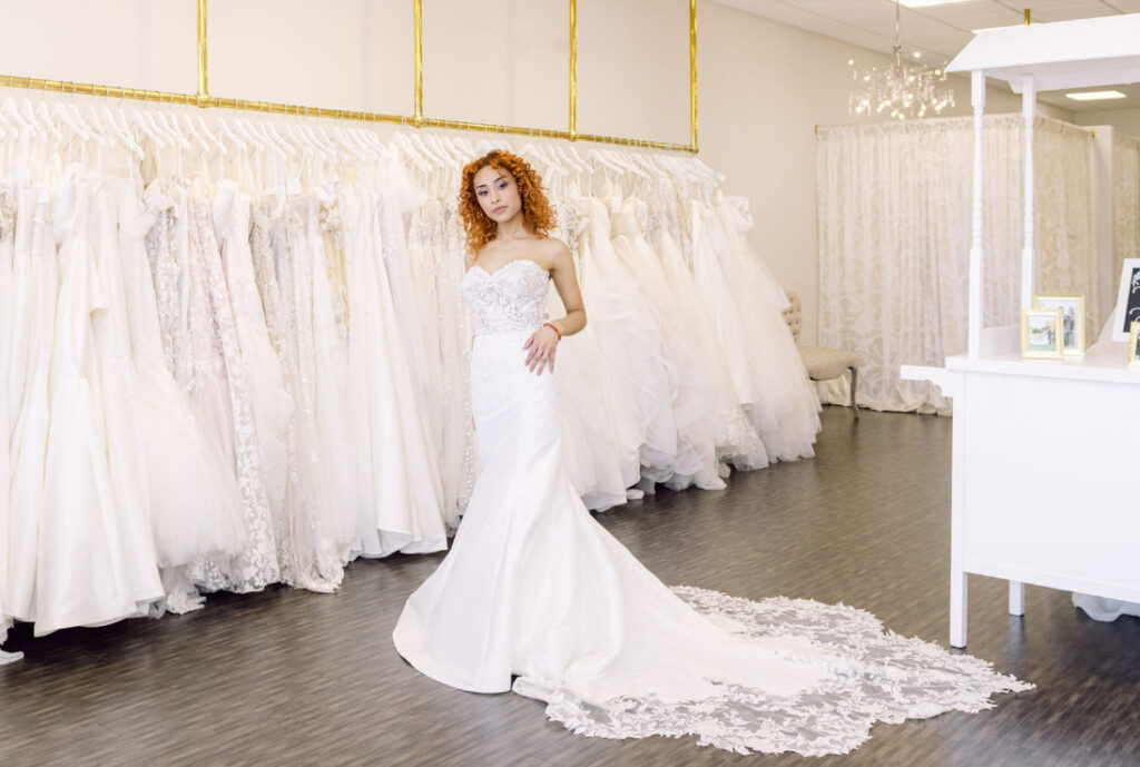 Bride with curly red hair posing in her wedding gown. The lace train of her gown is fanned out behind her.