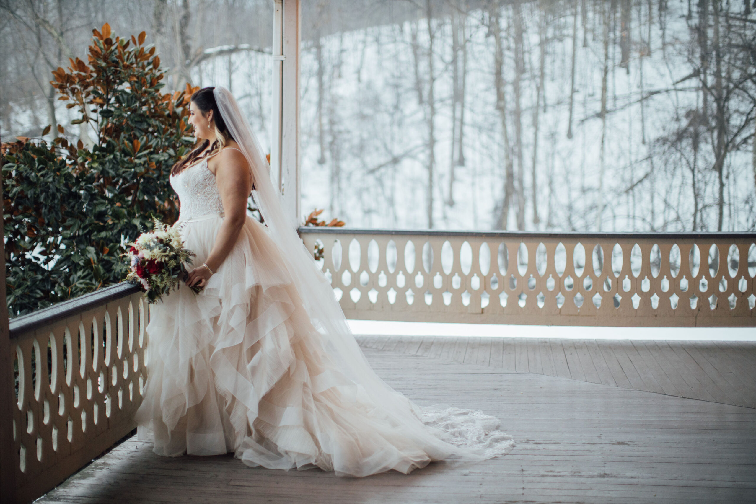 Plus sized bride wearing beautiful cream colored wedding dress with layering on the skirt. Bride has a long veil and is holding a winter colored bouquet.