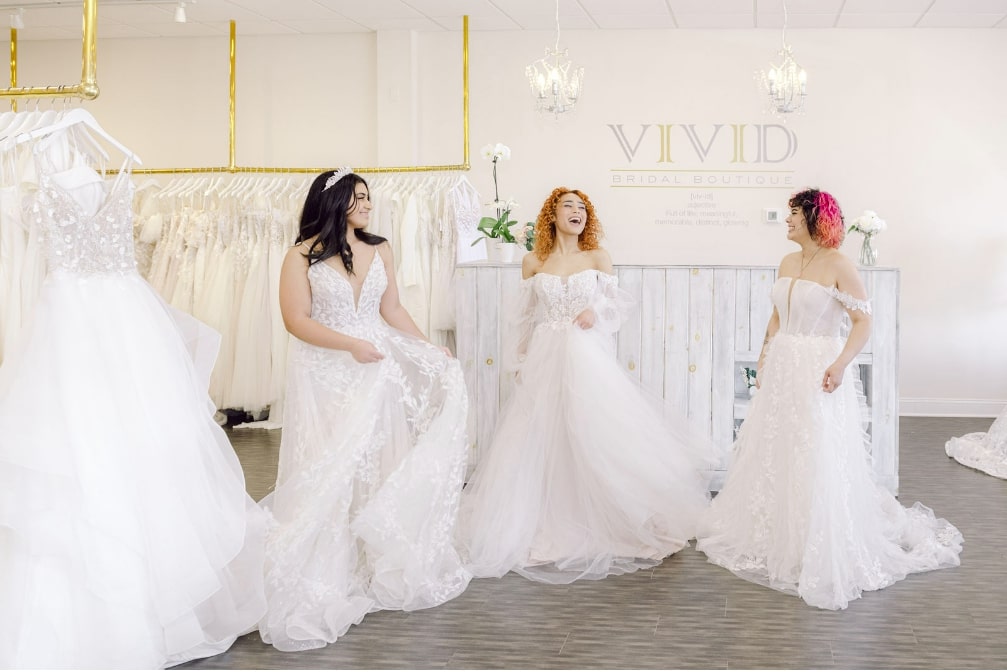 three brides-to-be laughing at Vivid Bridal Boutique wearing beautiful wedding dresses