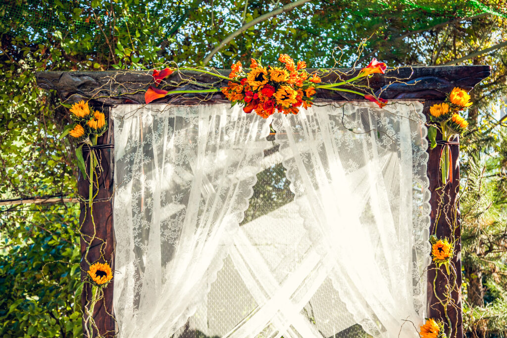 wooden arch decorated with white lace and orange, yellow, and red flowers