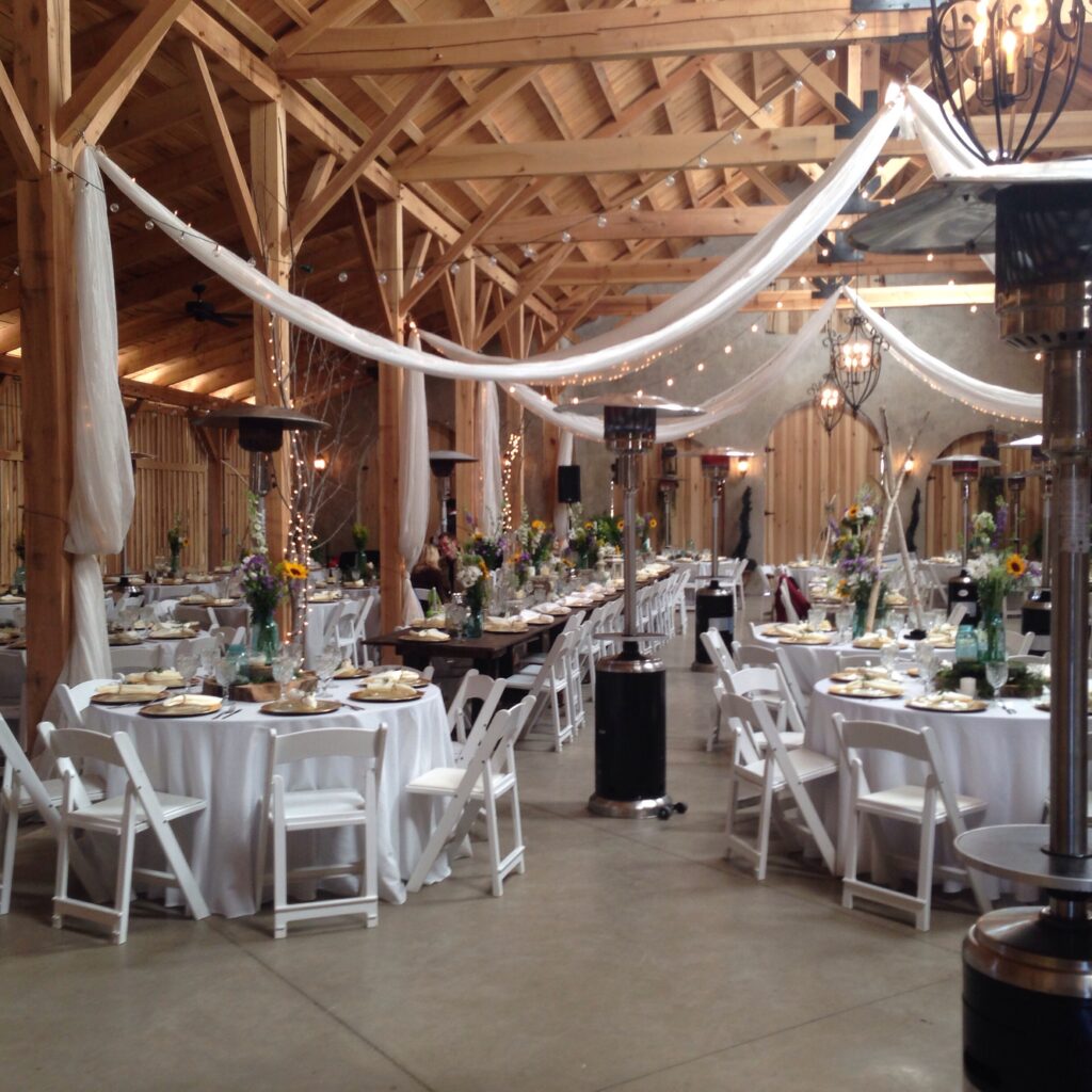 barn venue for a fall wedding with white cloth draped from the rafters above tables set with white tablecloths
