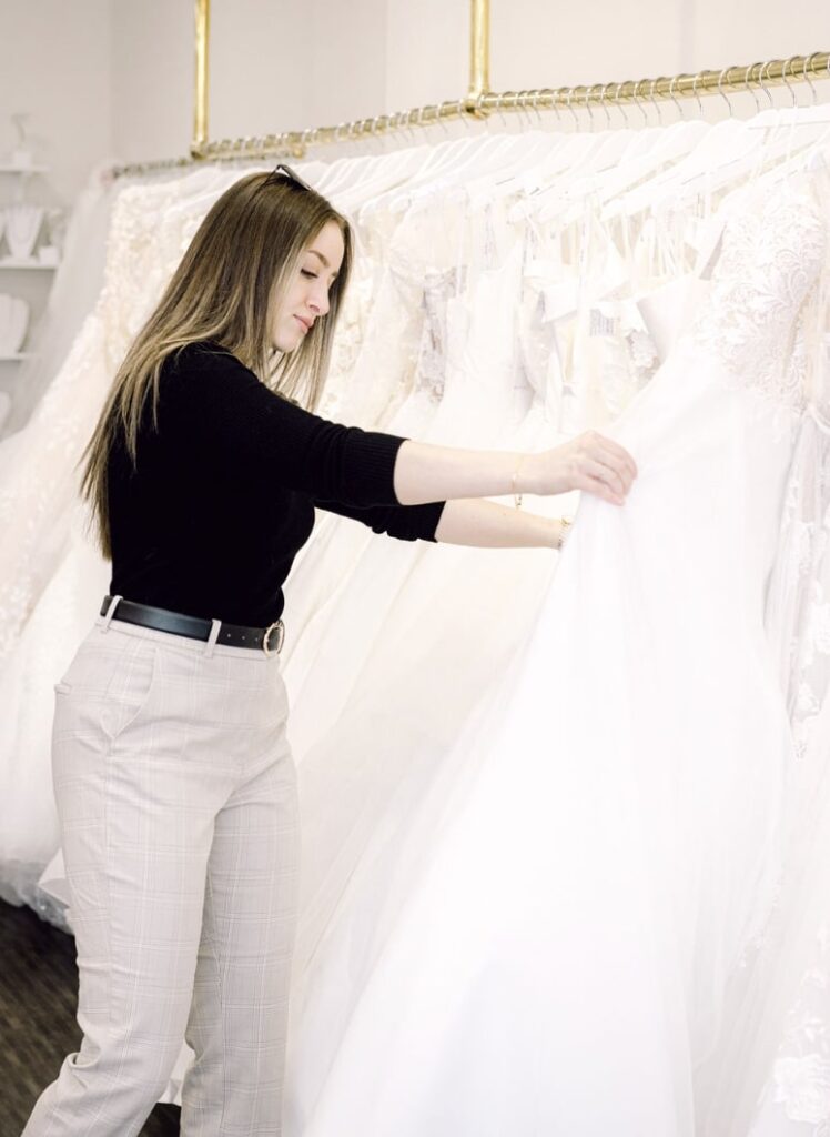 woman in black top browses wedding dresses on a rack at Vivid Bridal Boutique