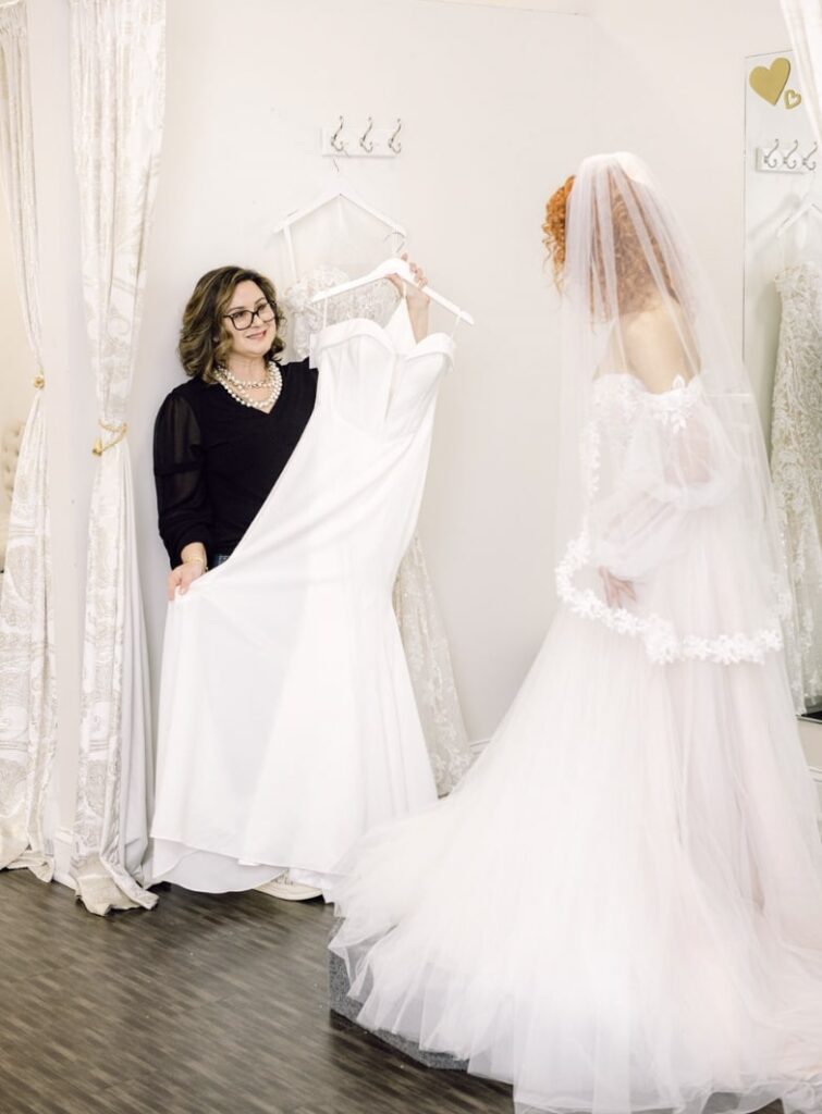 a woman in a black top shows a bride a potential wedding gown at Vivid Bridal Boutique