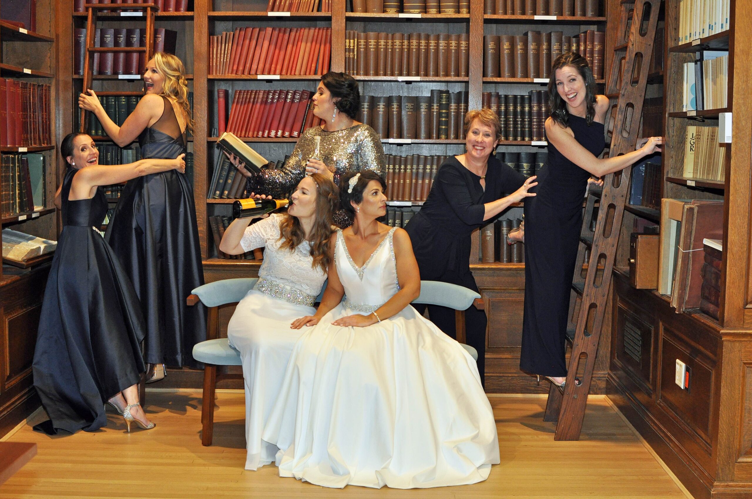 Teacher Bride-to-Be sitting on a bench in a library with her bridesmaids surrounding her.