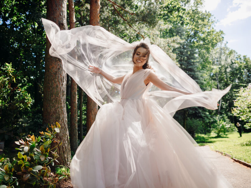 Bride wearing light pink, flowy wedding dress and twirling in circles. The bride's veil is floating in the air around the bride.