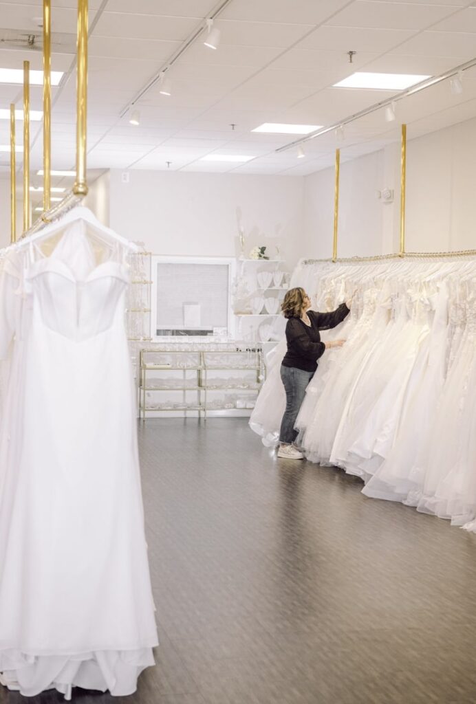 woman in a black top checking on a white wedding dress hanging on a gold rack