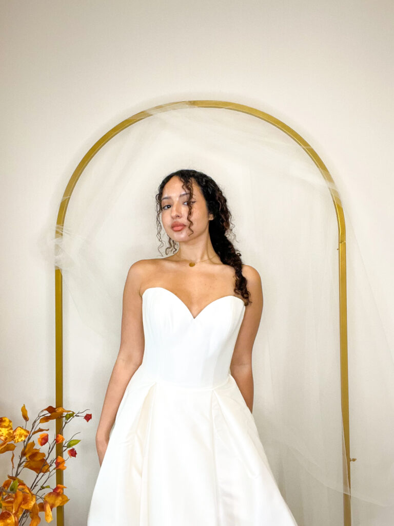 bride standing in front of a golden arch wearing a classic, white wedding dress